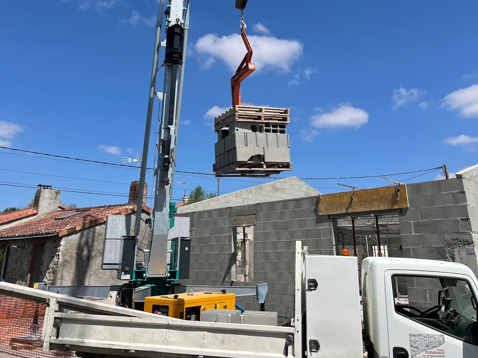 Grue de chantier Fleurance Maçonnerie levant une palette de parpaings au-dessus des murs en construction