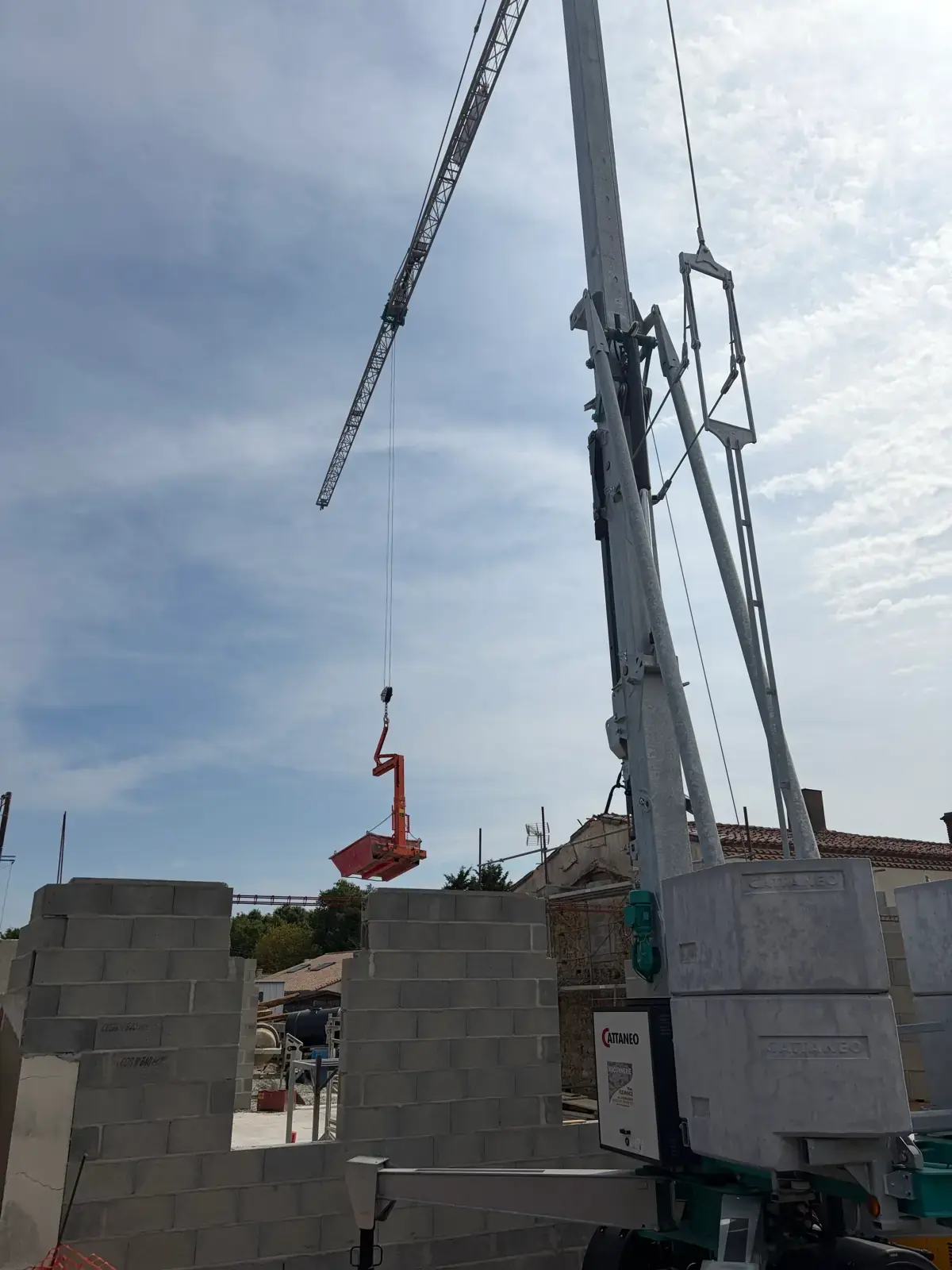 Fourche à palettes suspendue à la grue au-dessus des murs en parpaings fraîchement montés