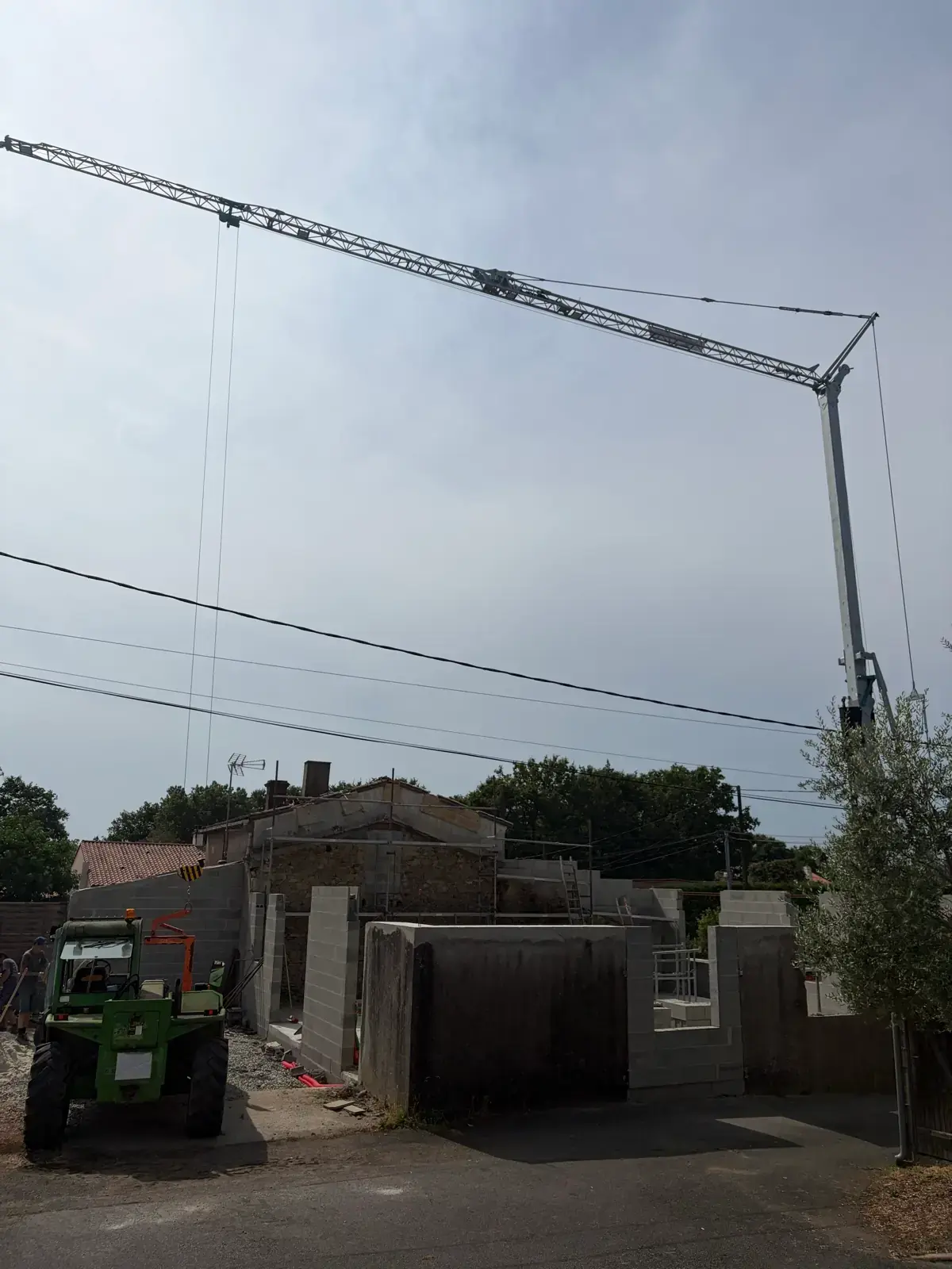 Murs en parpaings en cours d'élévation sous la flèche de la grue automontante, chariot télescopique en arrière-plan
